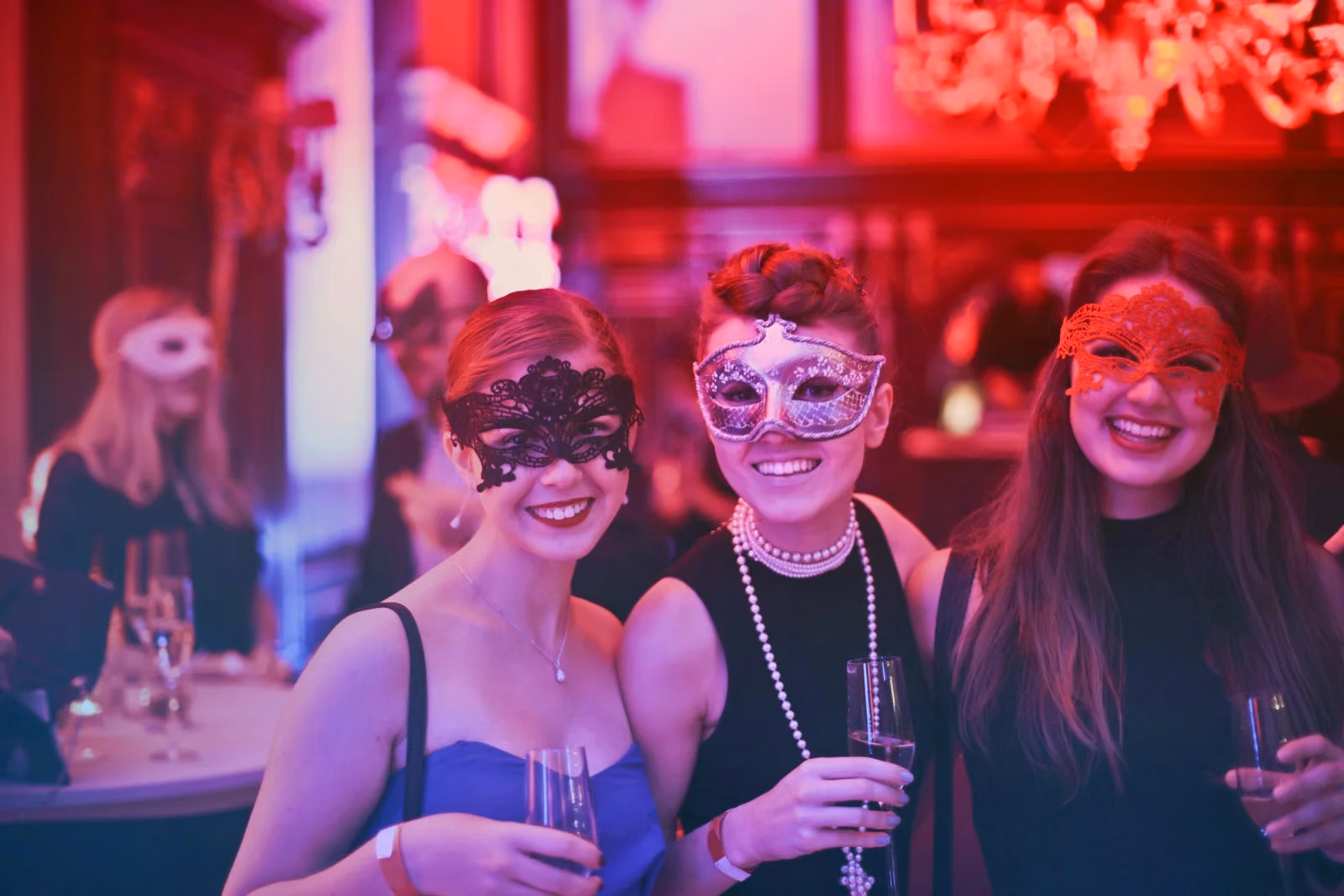 Three women wearing decorative masks stand together in a dimly lit bar.