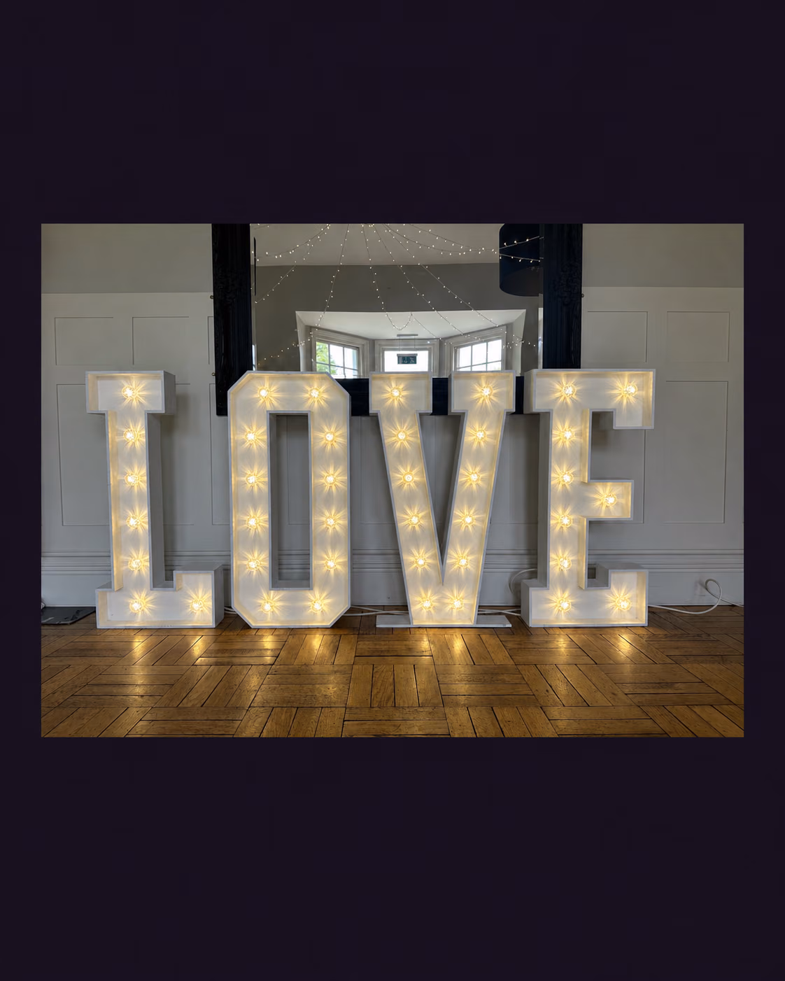 White illuminated LOVE letters displayed in front of a wall mirror.
