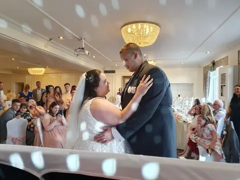 A wedding couple dancing in a daylight-filled reception room while guests watch.