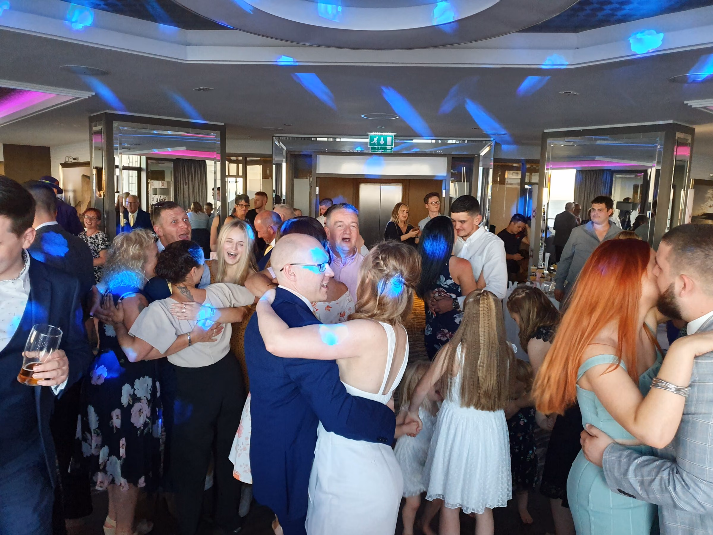 Wedding guests dancing together under blue party lights.